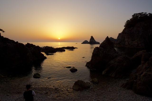 日本海の水平線に沈む夕日を眺める【pixta】
