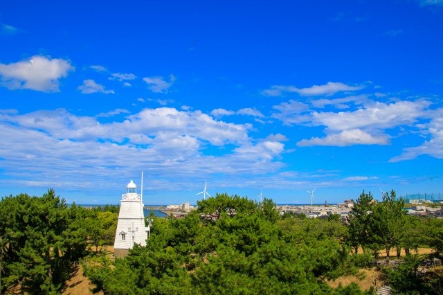 青空に映える公園の緑と白亜の灯台【AdobeStock】